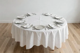 Table ronde dressée pour 10 personnes avec une nappe en lin blanc bien ajustée, vue en légère plongée dans une salle à manger scandinave
